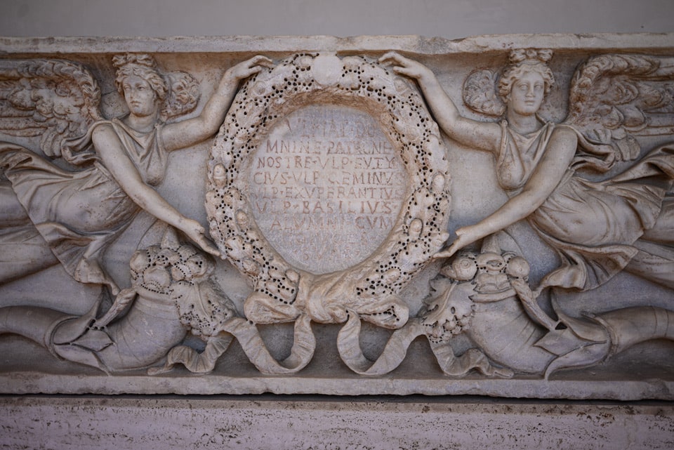 Antikes römisches Marmorrelief mit geflügelten Viktorien, die einen beschrifteten Kranz halten, im Kreuzgang der Diokletiansthermen in Rom